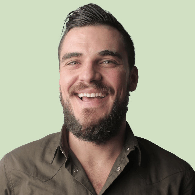 Man with a beard and short hair smiling against a light green background