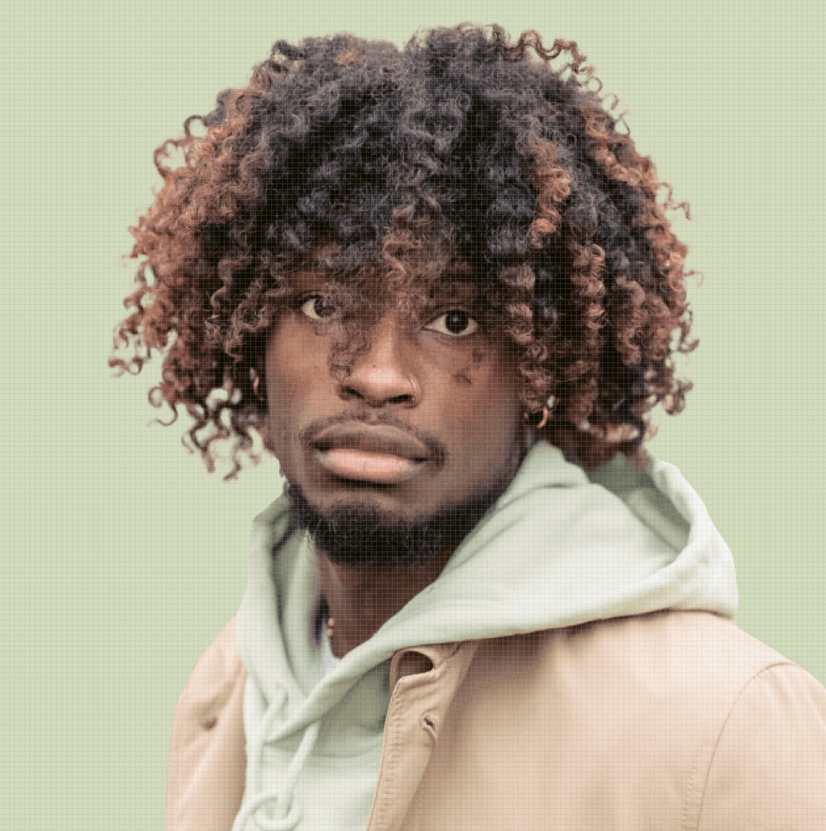 Man with curly hair wearing a light-colored hoodie and jacket against a green background
