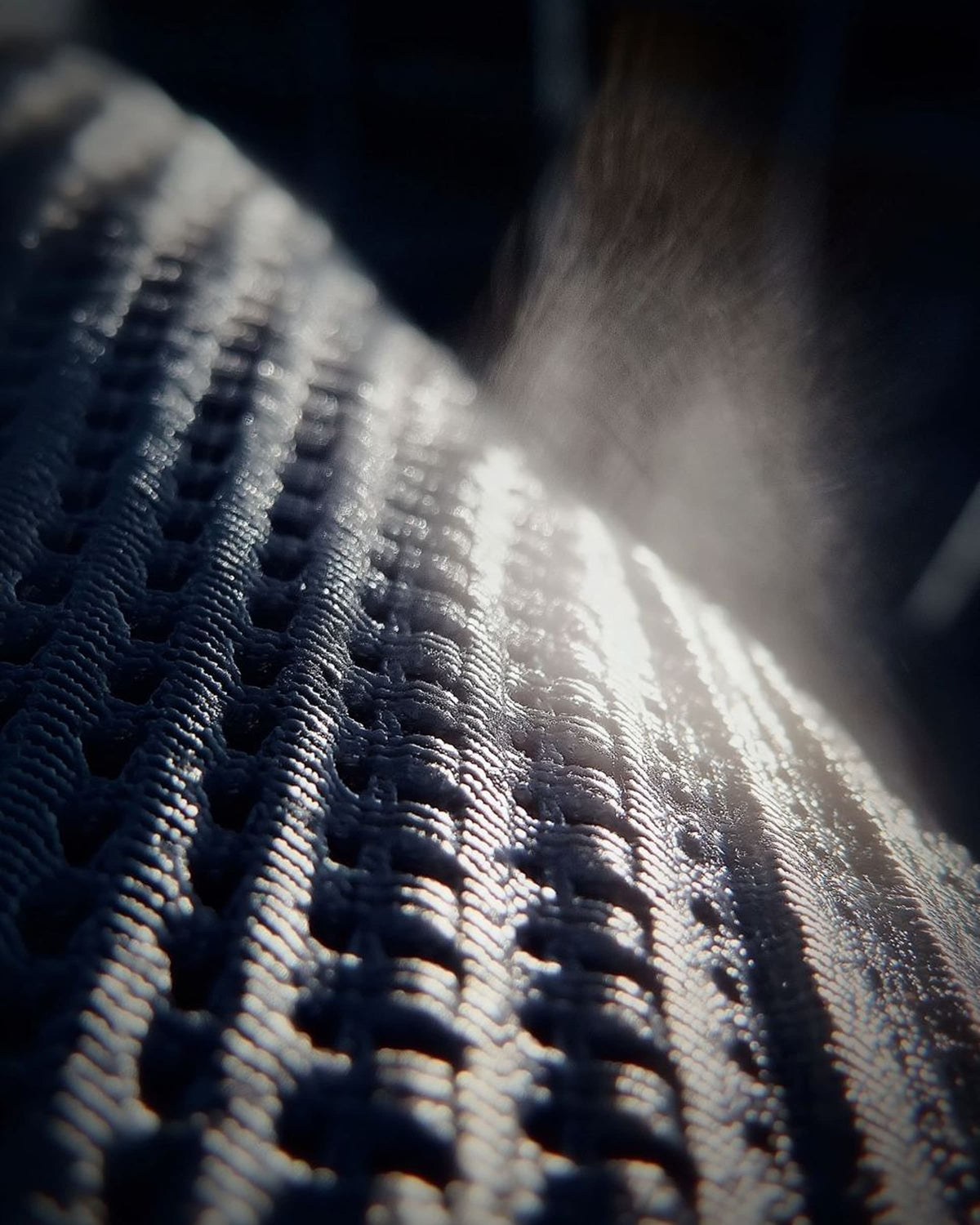 An extreme close-up of textured, perforated athletic fabric with rows of raised ridges and small holes, lit dramatically to highlight the material’s breathable weave and surface detail.